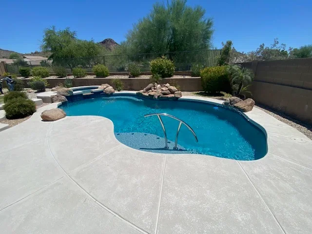 Freeform pool with spa, stamped concrete deck, and rock features