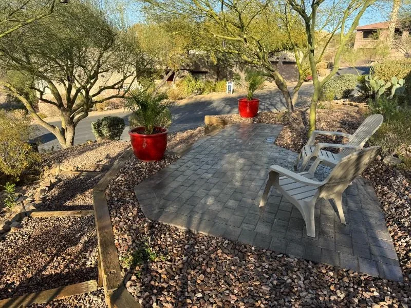 Paver patio with lounge chairs, desert trees, river rock mulch, and red planters