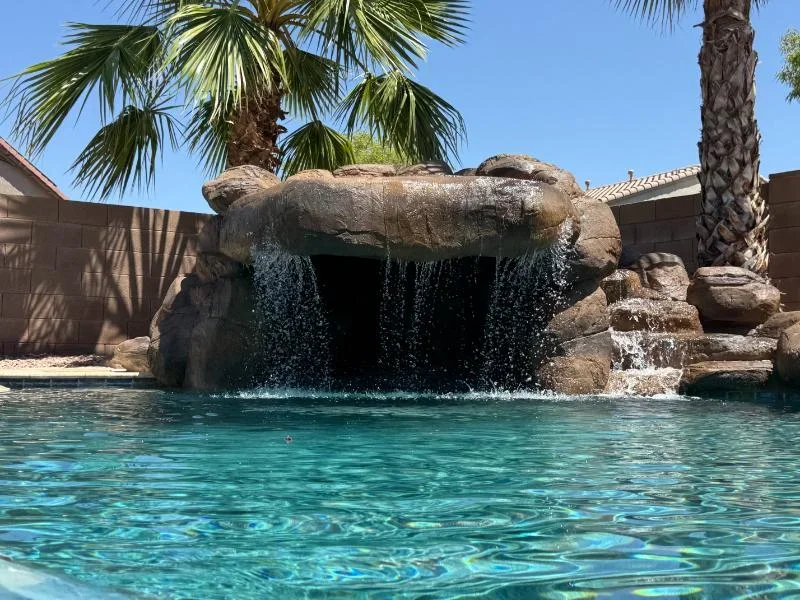 Stacked boulder waterfall with multiple water streams flowing into turquoise pool water