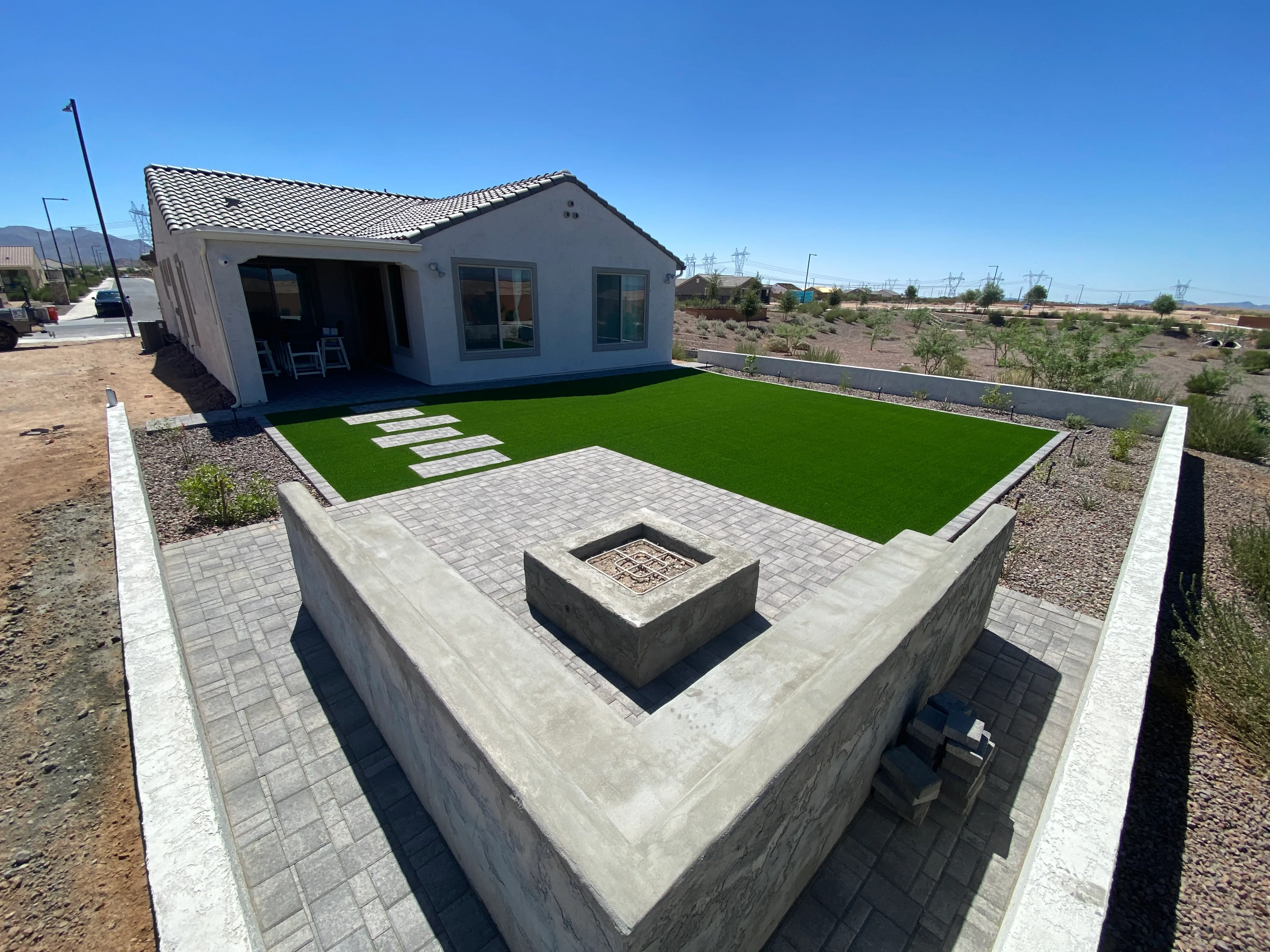 Paver patio with fire pit, synthetic turf lawn, concrete retaining walls, and landscape edging
